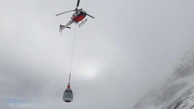 Im Bild fliegt ein Hubschrauber ein O'Bellx-Gerät auf den Berg.