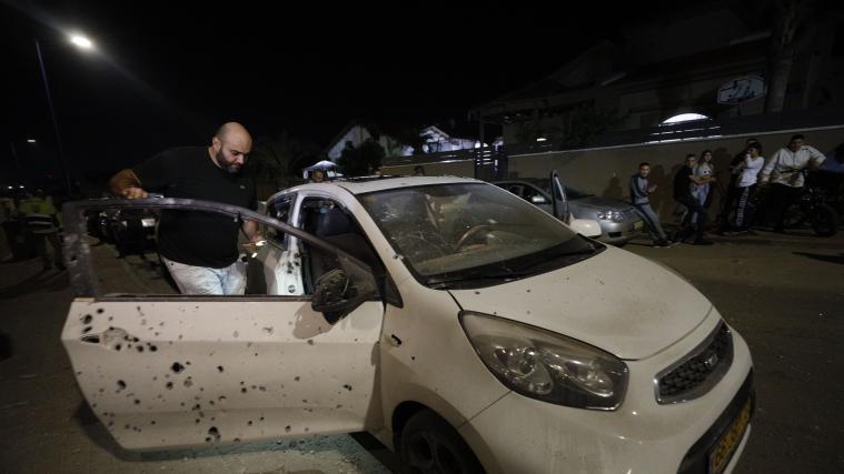 Ein Mann begutachtet ein durch eine Rakete beschädigtes Auto.