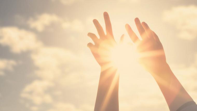 Die Hände einer Frau greifen zum Himmel und zur Sonne
